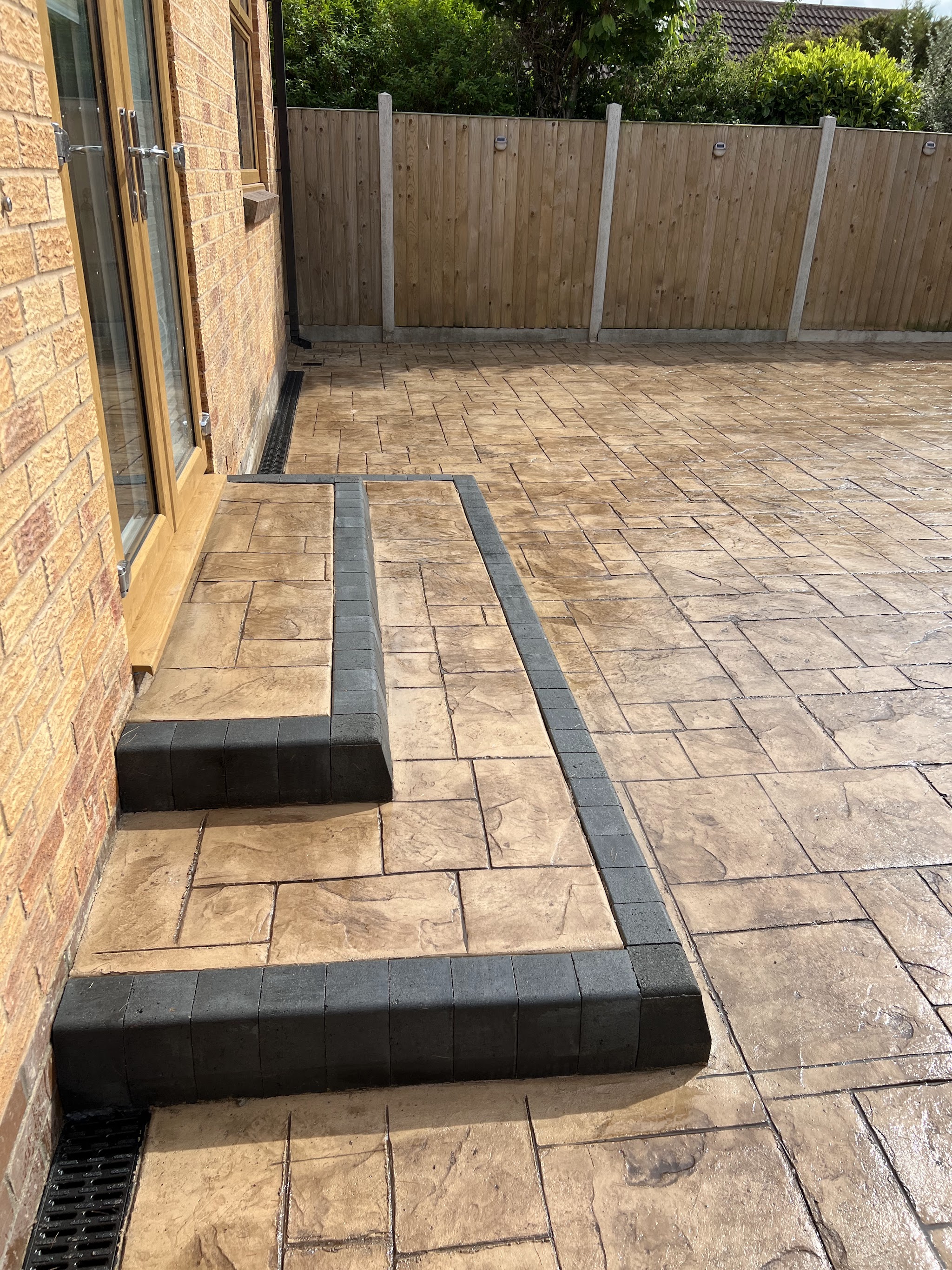 Buff printed patio with dark edged steps and a drainage channel