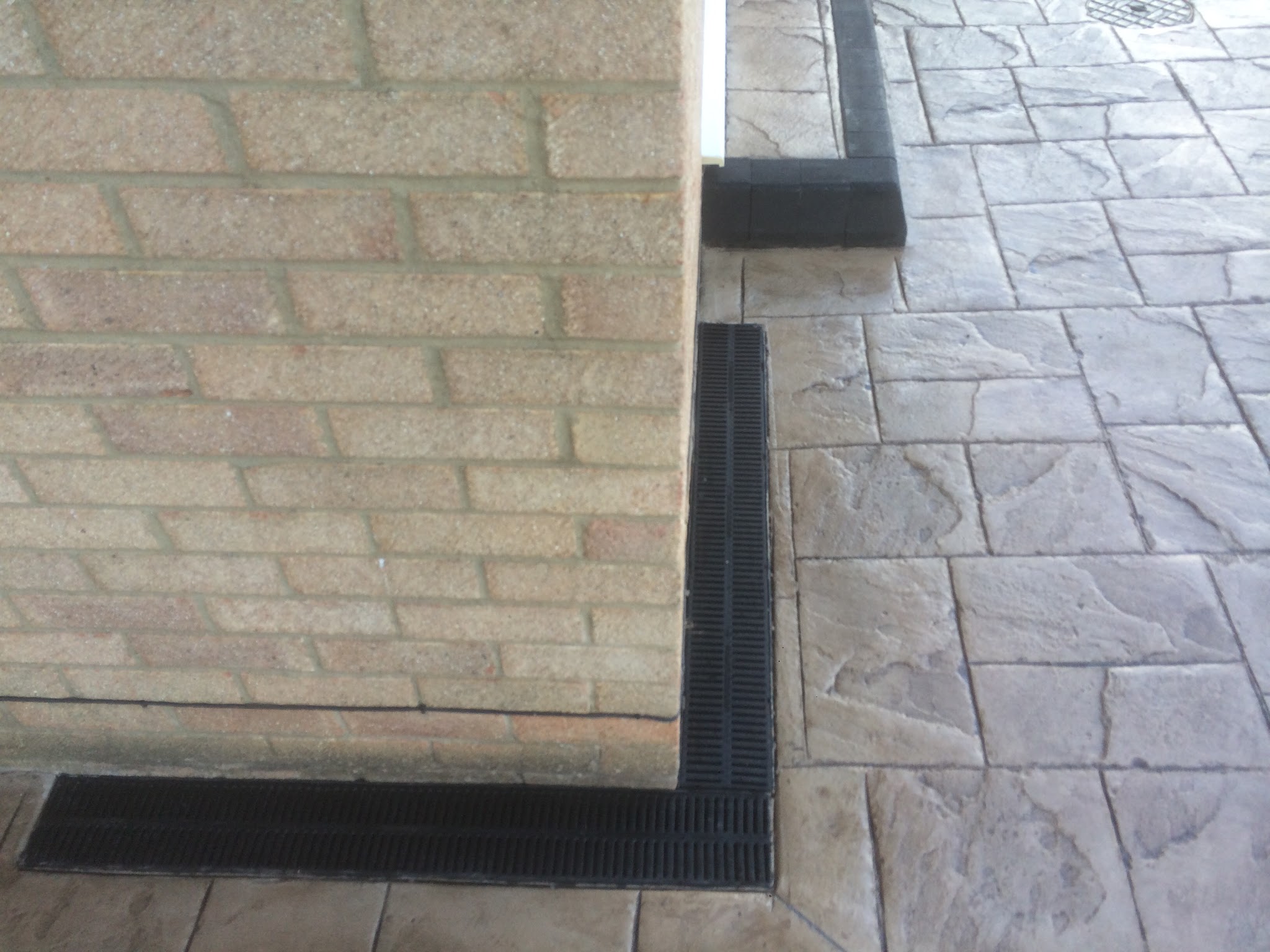 Close-up of a light printed path with a dark border and drainage channel at the corner of a house